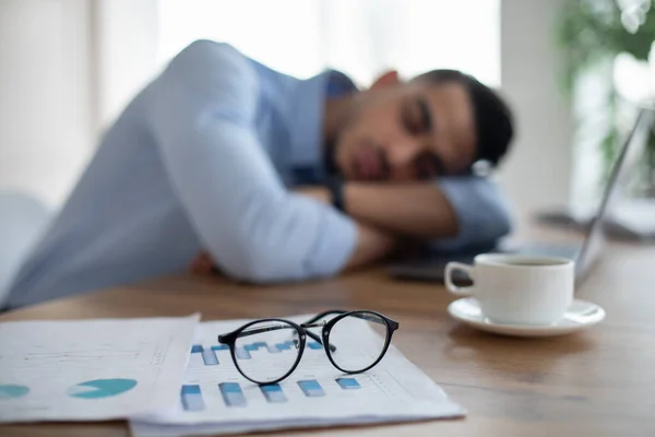 Uitgeputte Arabische zakenman slaapt op zijn bureau, moe van overwerken, selectieve focus op documenten en glazen — Stockfoto