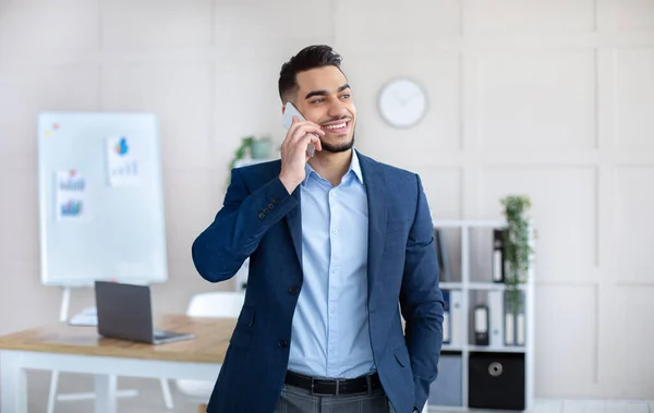 Positieve jonge Arabische man in pak in gesprek op mobiele telefoon op het werk — Stockfoto