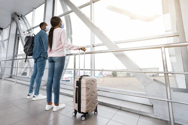 Viajes de cuarentena. Pareja negra en máscaras médicas esperando el vuelo en el aeropuerto — Foto de Stock