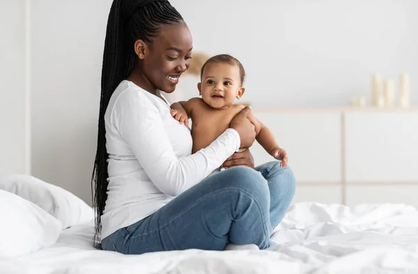 Preto babá sentado no cama com ela bonito bebê — Fotografia de Stock