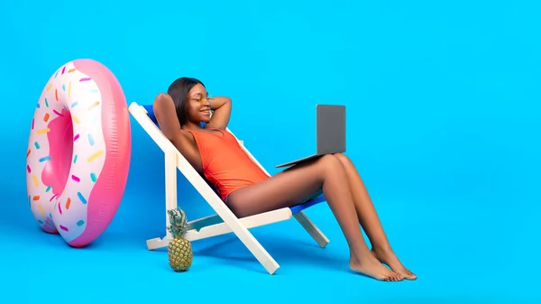 Siyah kadın dizüstü bilgisayarla şezlongda takılıyor, plaj cennetinden sohbet ediyor, yaz tatilinde film izliyor. — Stok fotoğraf