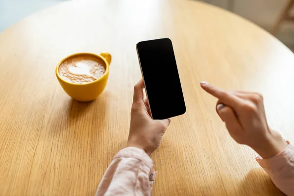 Добрий початок дня. Молода леді тримає смартфон з порожнім екраном і п'є ранкову каву, сидячи в кафе — стокове фото