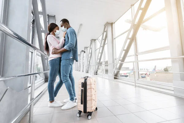 Viagens pandémicas. Jovem casal negro em máscaras médicas abraçando no aeroporto — Fotografia de Stock