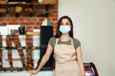 Covid-19 karantinasında yeni normal, yeni başlayan ve küçük işletmeler. Önlüklü ve koruyucu maskeli Latin bayan barista.