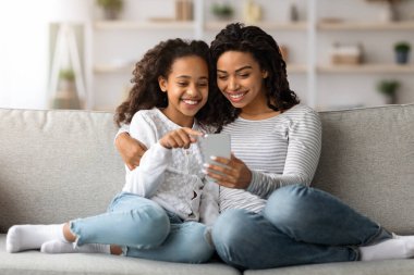 Neşeli Afro-Amerikan annesi ve kızı akıllı telefonu birlikte kullanıyorlar.