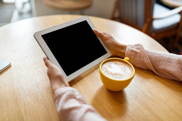 Ugjenkjennelig dame som bruker digital nettbrett med blank skjerm, som har videosamtale mens hun sitter på kafe og drikker kaffe – stockfoto