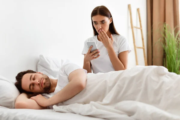 Esposa sorprendida leyendo mensaje sobre infiel maridos Smartphone en el dormitorio — Foto de Stock