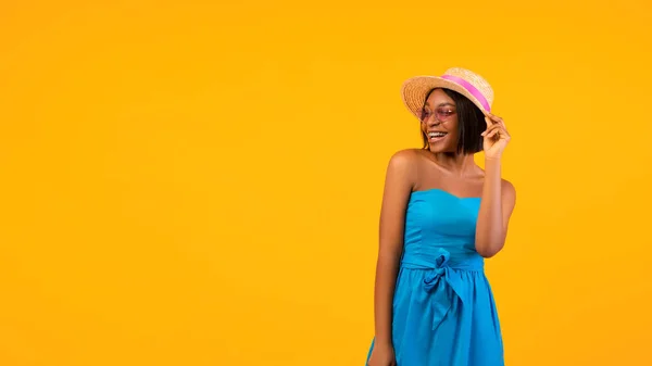 Mujer negra feliz en vestido de verano y sombrero de paja mirando a un lado en el espacio vacío sobre fondo naranja, diseño de la bandera — Foto de Stock