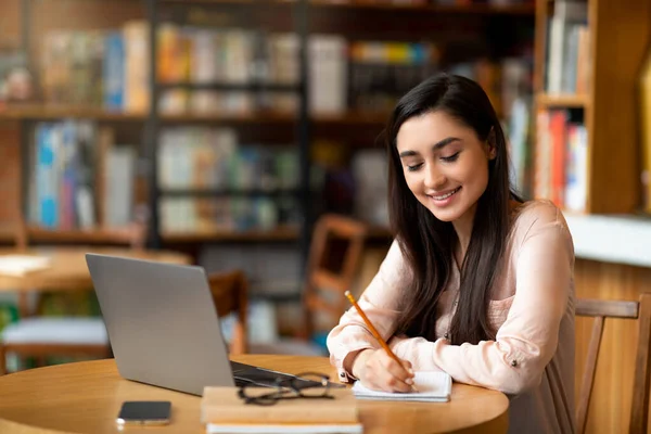 Educación en línea. Mujer latina motivada estudiando con laptop en la cafetería y tomando notas mientras ve webinar — Foto de Stock