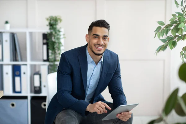 Schöner arabischer Geschäftsmann im formellen Anzug mit Tablet-PC am Arbeitsplatz, der im Büro Web-Dokumente durchblättert — Stockfoto