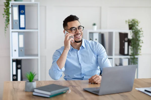 Bello giovane arabo in abito formale parlando su smartphone, godendo di conversazione sul posto di lavoro — Foto Stock