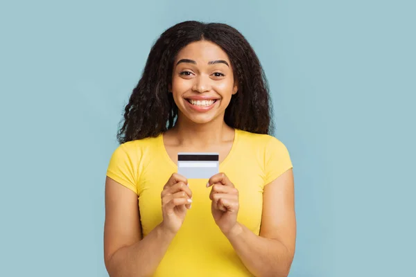Концепція легкої оплати. Захоплена афро - американка, яка тримає дебетову кредитну картку над синім фоном студії — стокове фото