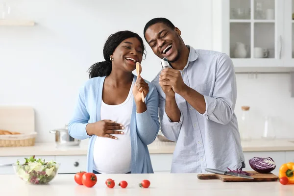 Positivo grávida preto casal cantando enquanto cozinha — Fotografia de Stock