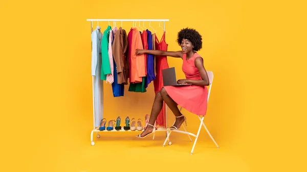 African Woman Using Laptop Shopping Online Choosing Clothes, Yellow Background