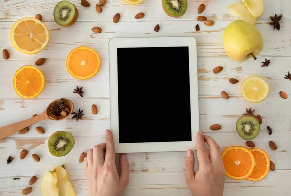 Healthy nutrition concept. Female hands holding digital tablet with black screen on table with fruit slices, top view — Stock Photo, Image