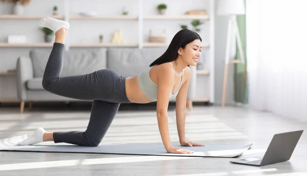 Hacer ejercicio en casa. Deportiva asiática mujer haciendo ejercicio en línea con el ordenador portátil —  Fotos de Stock