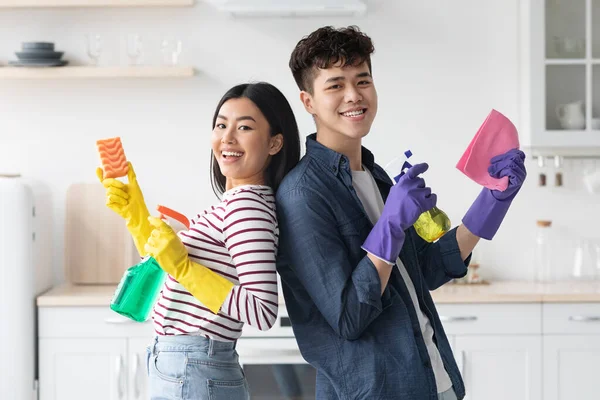 Cheerful asian couple with supplies for cleaning posing in kitchen — Stock Photo, Image