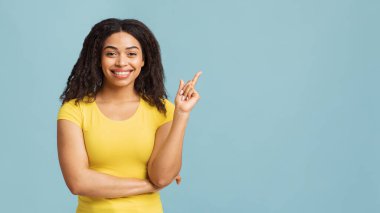 Şuraya bak. Mavi stüdyo arka planında boş bir yeri işaret eden mutlu siyahi kadın bir şey öneriyor.