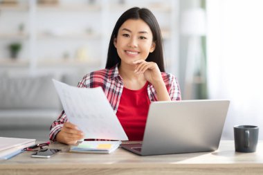 Mesafe işi. Asyalı serbest çalışan kadın evde bilgisayar ve kağıtlarla çalışıyor.