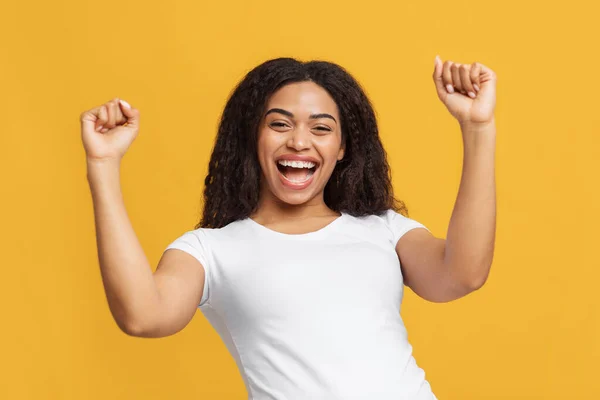 Ganar concepto. Alegre dama afroamericana celebrando la victoria y sacudiendo los puños apretados en el fondo amarillo del estudio — Foto de Stock