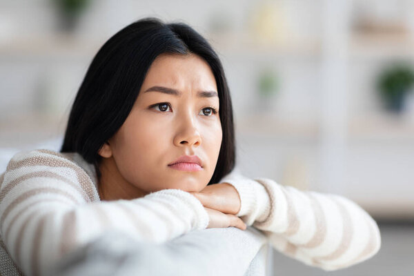 Depression Concept. Closeup Of Upset Asian Female Sitting On Couch At Home
