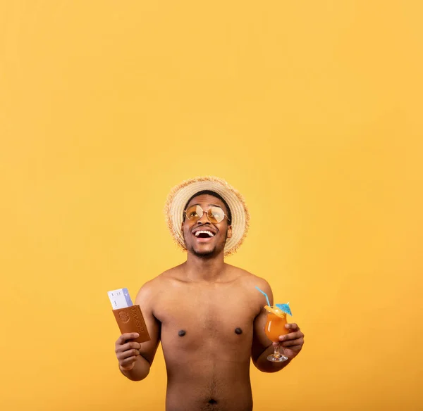 Chico negro fresco con pecho desnudo sosteniendo cóctel de frutas, pasaporte y boletos de avión, ir de vacaciones a país tropical —  Fotos de Stock