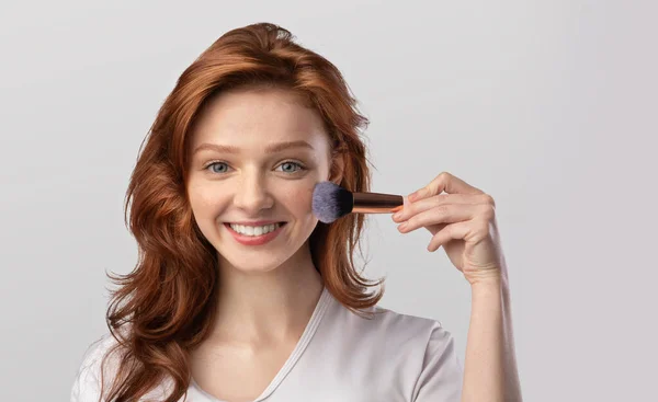 Ingwerhaarige junge Dame posiert mit Kosmetikbürste im Studio — Stockfoto
