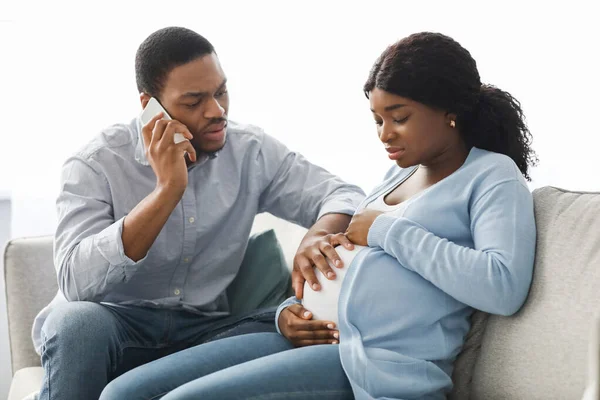 Zmartwiony czarny mąż wzywa lekarza podczas gdy żona ma bóle porodowe — Zdjęcie stockowe