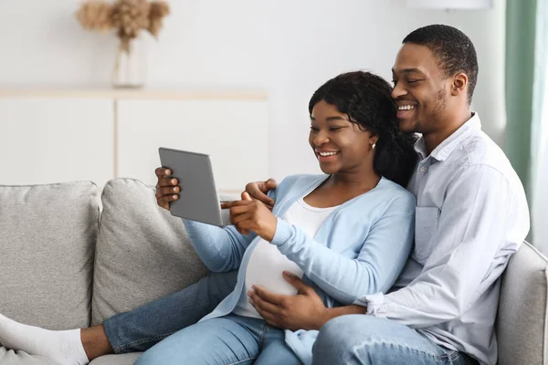 Wesoła ciężarna para czarnych za pomocą tabletu cyfrowego w domu — Zdjęcie stockowe