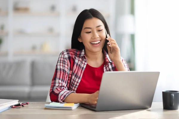 Telewerken. aziatische vrouw praten op mobiele telefoon en werken met laptop thuis — Stockfoto