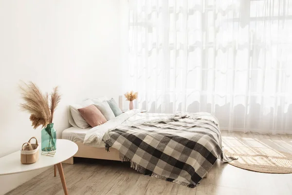 Легкий стиль и дизайн недвижимости. Кровать с подушками и одеялом, ковер, столы с сухими растениями в вазах — стоковое фото