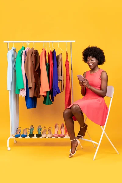 Senhora afro-americana positiva usando roupas de compra de celular, fundo amarelo — Fotografia de Stock