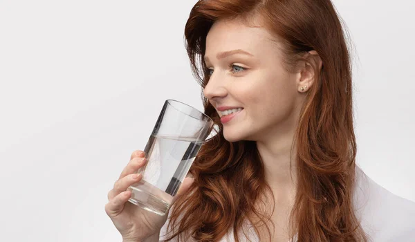 Vista lateral de la chica pelirroja bebiendo agua sobre fondo blanco —  Fotos de Stock