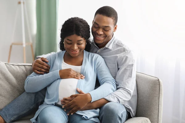 흑인 남자가 임신 한 여자를 껴안고 소파에 앉아서 — 스톡 사진