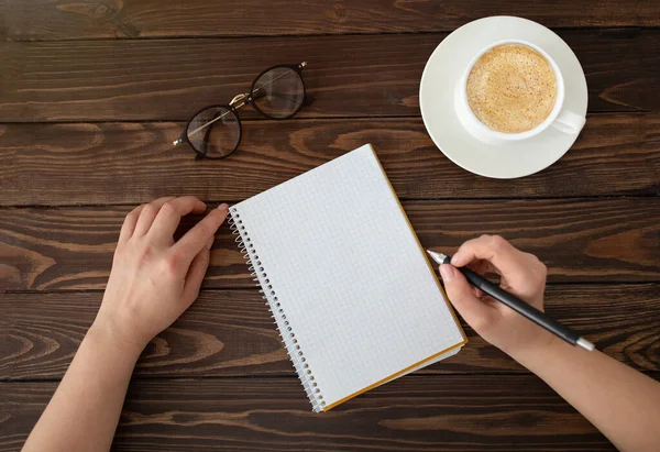 Objetivos ou conceito de escrita de planos. Mulher com caderno vazio e xícara de café, sentado em mesa de madeira escura, vista superior — Fotografia de Stock