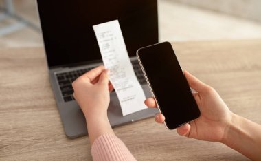 Boş ekranı ve faturası olan akıllı telefonu tutan kadın eller, iş yerinde dizüstü bilgisayarla oturuyor.