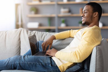 Rahat siyah adam dizüstü bilgisayar kullanıyor, boş ekran, ev içi.