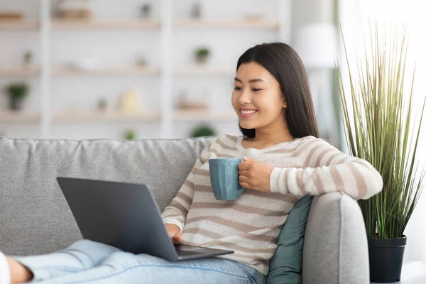 Favoriete vrije tijd. gelukkig aziatische vrouw ontspannen thuis met laptop en koffie — Stockfoto