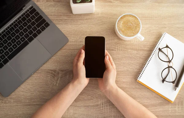 Mujer sosteniendo teléfono inteligente con pantalla vacía para su diseño o anuncio, fondo de mesa de madera, vista superior — Foto de Stock