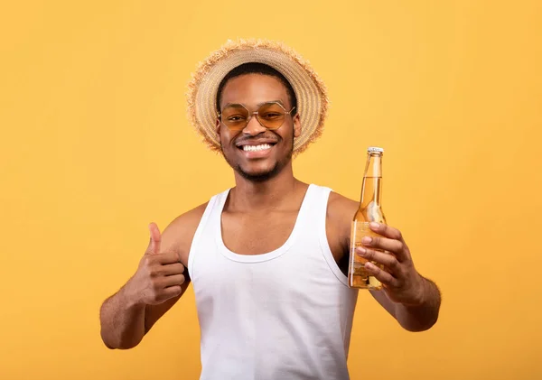 Jóképű fekete srác nyári ruhákban kezében üveg sör és gesztikuláló hüvelykujj fel sárga stúdió háttér — Stock Fotó