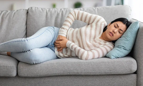 Pijn van de menstruatie. jong aziatische vrouw lijden van acute maag pijn thuis — Stockfoto