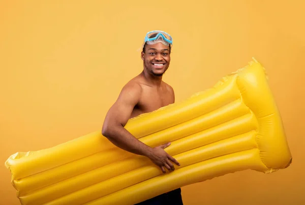 Şnorkel maskeli gülümseyen siyah adam şişme lilo taşıyor, sarı arka planda kumsala gidiyor. — Stok fotoğraf