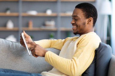 Kanepede dijital tabletle dinlenen neşeli siyahi adam.