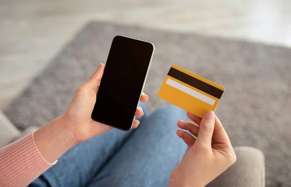 Online vásárlási koncepció. Nő tart hitelkártya és okostelefon üres képernyőn, ül a kanapén otthon — Stock Fotó