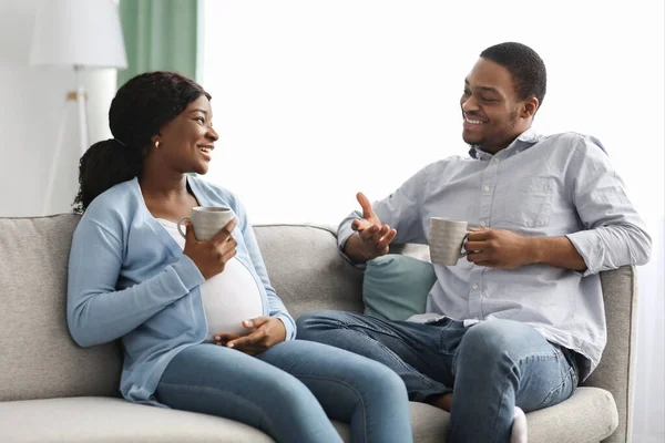 Радостная ожидающая черная пара, сидящая на диване, пьющая чай — стоковое фото