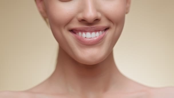 Primer plano de la mujer sonriendo a la cámara, mostrando una sonrisa blanca de después del procedimiento de alineación de los dientes, fondo beige — Vídeo de stock