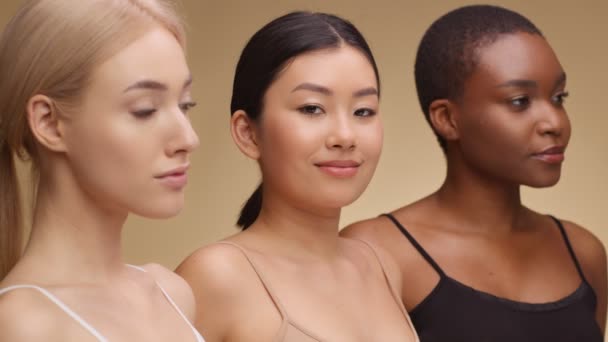Wanita Asia muda yang lucu tersenyum ke kamera, berpose dengan Kaukasia dan african teman-teman Amerika atas latar belakang studio beige — Stok Video