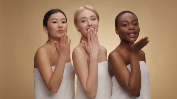 Studio portret van drie speelse multi-etnische dames sturen blow kusjes naar de camera, poseren verpakt in handdoeken — Stockvideo