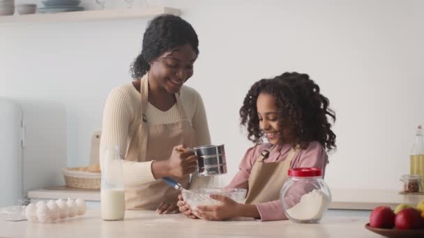 Giovane felice afro americano madre e figlia cottura a casa insieme, donna aggiungendo farina con setaccio in ciotola — Video Stock