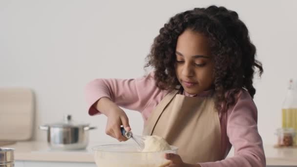 Graziosa ragazza afroamericana che gioca con la pasta cruda, guardandola versare dalla frusta in cucina, rallentatore — Video Stock